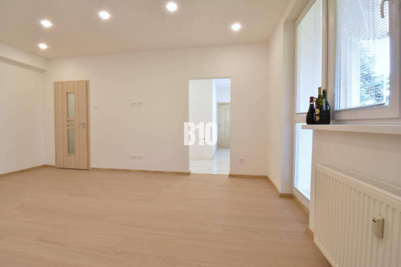 A bright room with wooden flooring in a 3-room apartment, illuminated by ceiling lights.