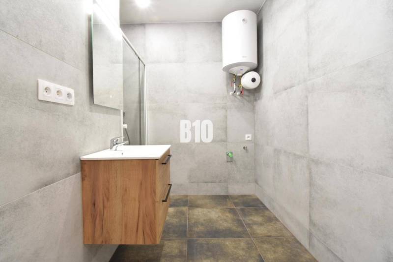 A bathroom in a 3-room apartment with a sink and a boiler, light tiles dominate the space.