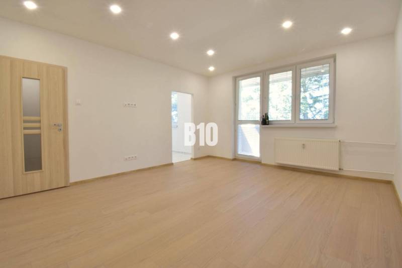 A bright room in a 3-room apartment with wooden flooring and a large window.