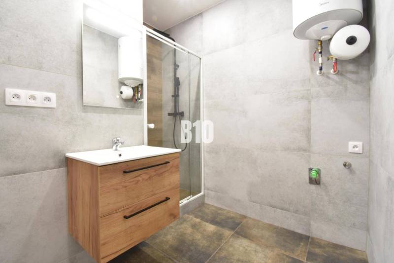 A bathroom in a 3-room apartment with a wooden cabinet, a shower corner, and a water heater.