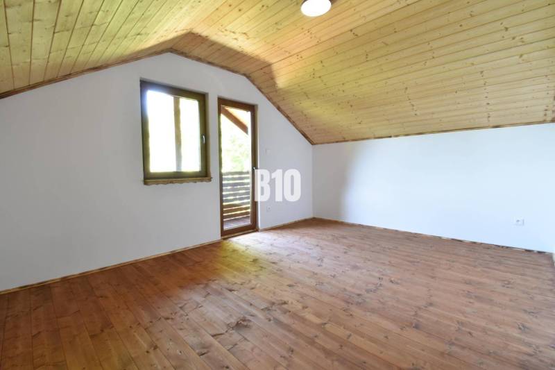 Attic spaces of the cottage with wooden floor and ceiling, window and door to the terrace.