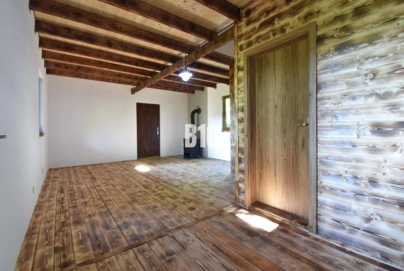 Interior of a cabin with wooden beams, flooring, and a stove for heating.