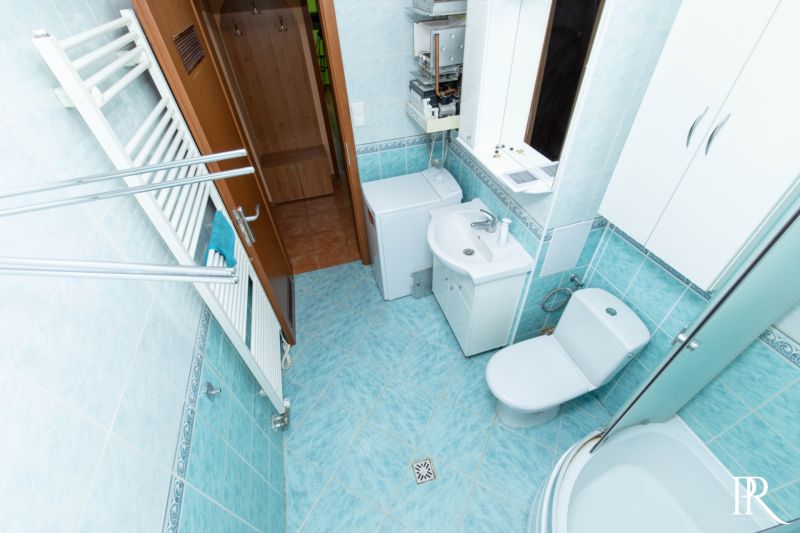 Bathroom in a 2-room apartment with a washing machine, shower, sink, and mirror.