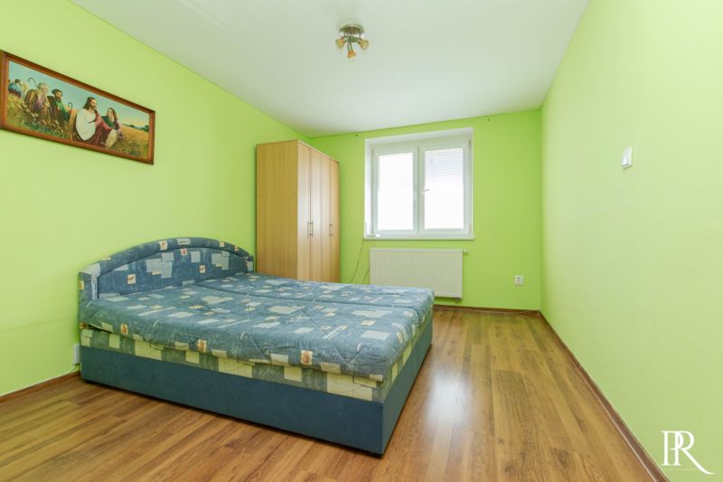 A bedroom with green walls, a double bed, and wooden flooring in a two-room apartment.