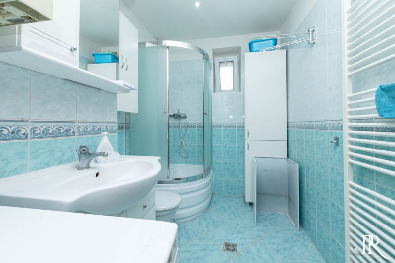 The bathroom in the 2-room apartment has a shower, a sink, cabinets, and white tiles.