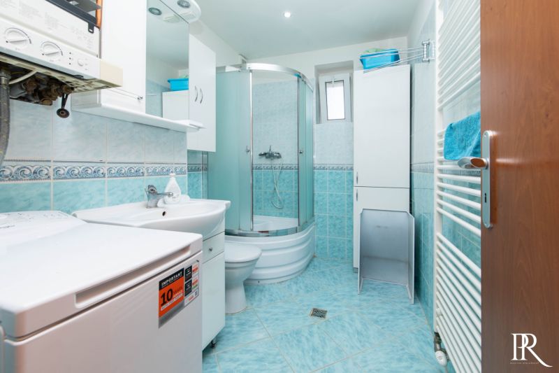 A bathroom with a washing machine and a shower in a 2-room apartment. Light tiles.