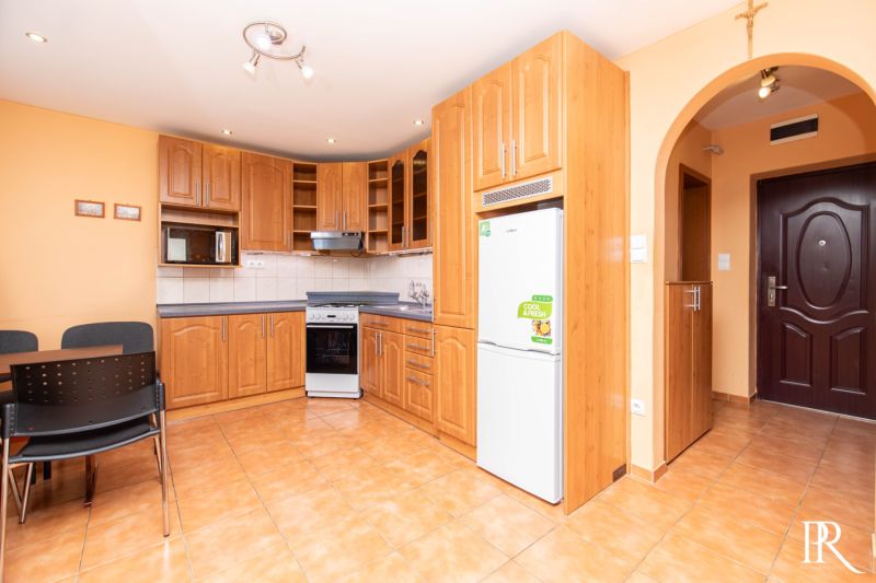 A kitchen in a 2-room apartment with a wooden cabinet, a microwave, and a stove on tiles.