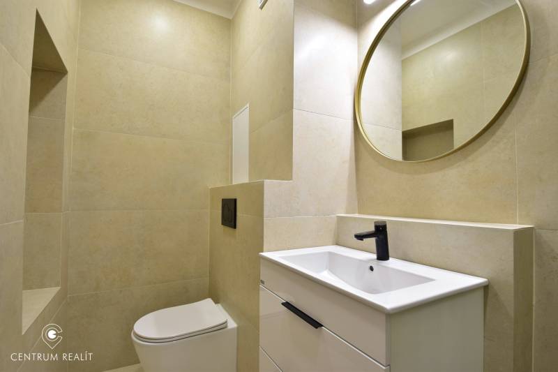 Bathroom in a 2-room apartment with a toilet, sink, black faucet, and round mirror.