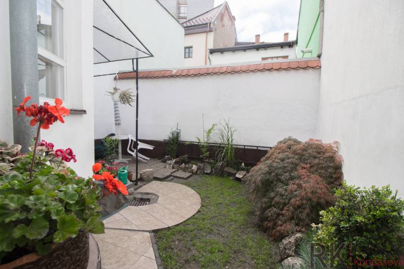 A small garden by a 2-room apartment with paving, plants, and stone decorations.