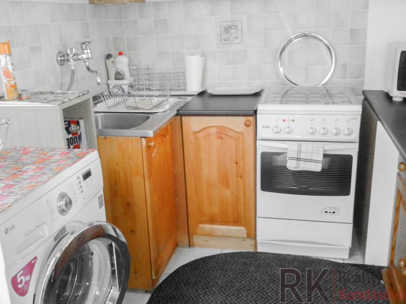 A kitchen in a 2-room apartment with a washing machine, stove, and wooden cabinets.
