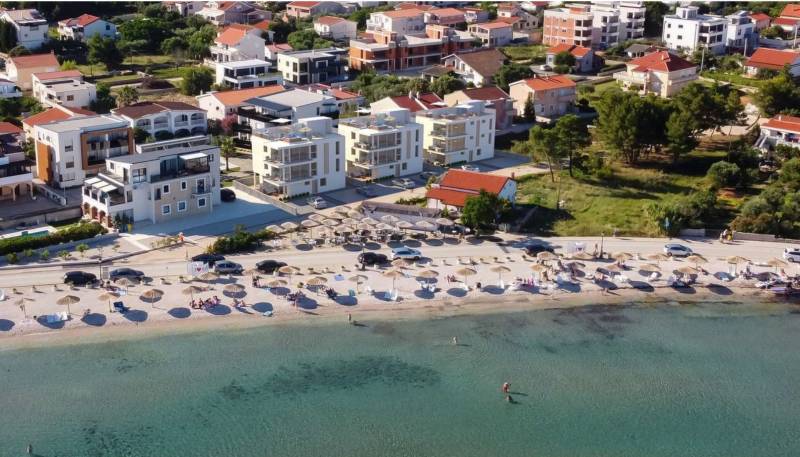A beach with sunbeds and umbrellas, behind it houses and buildings in the resort.
