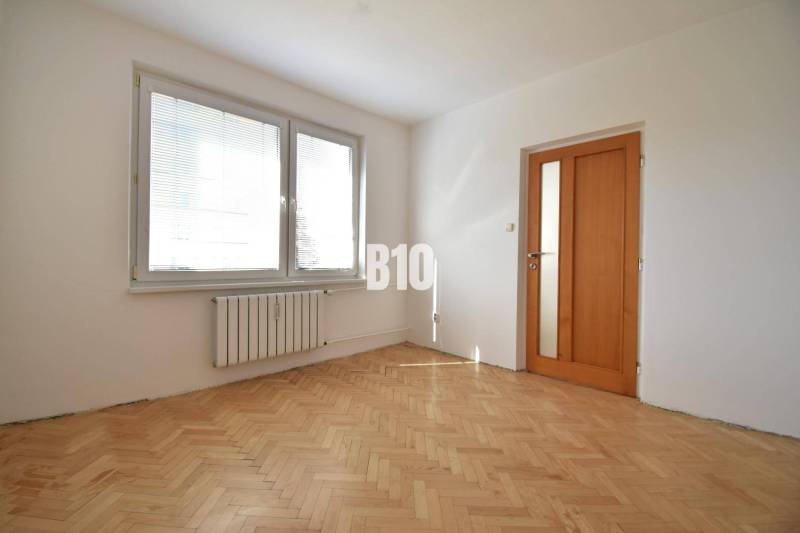 A room with parquet floors and windows with blinds in a 4-room apartment.