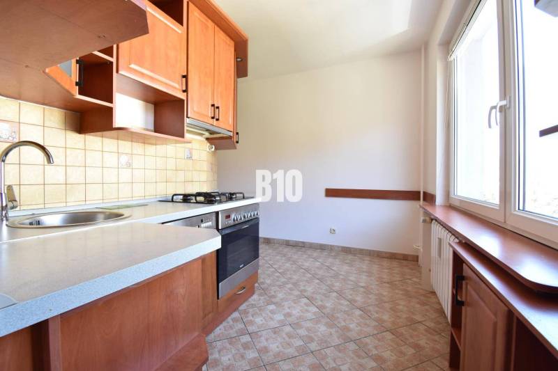 The kitchen of a 4-room apartment with a large window, wooden furniture, and tiles.