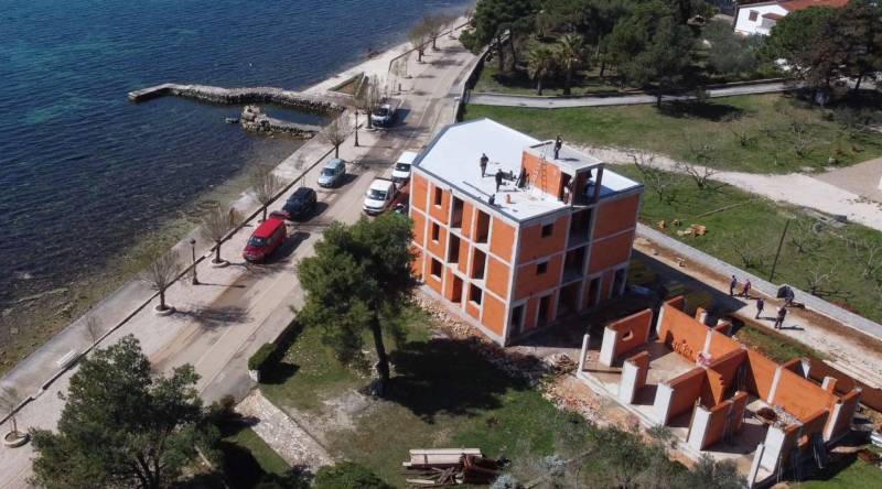 A building by the sea in the town of Vir with an access road and greenery.