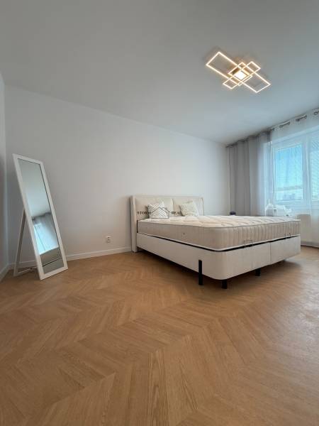 A bedroom in a 3-room apartment with a comfortable bed, stylish mirror, and patterned floor.