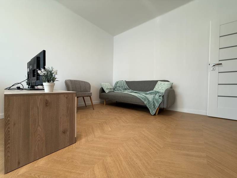 Living room in a 3-room apartment with a sofa, armchair, and television on a wooden cabinet.