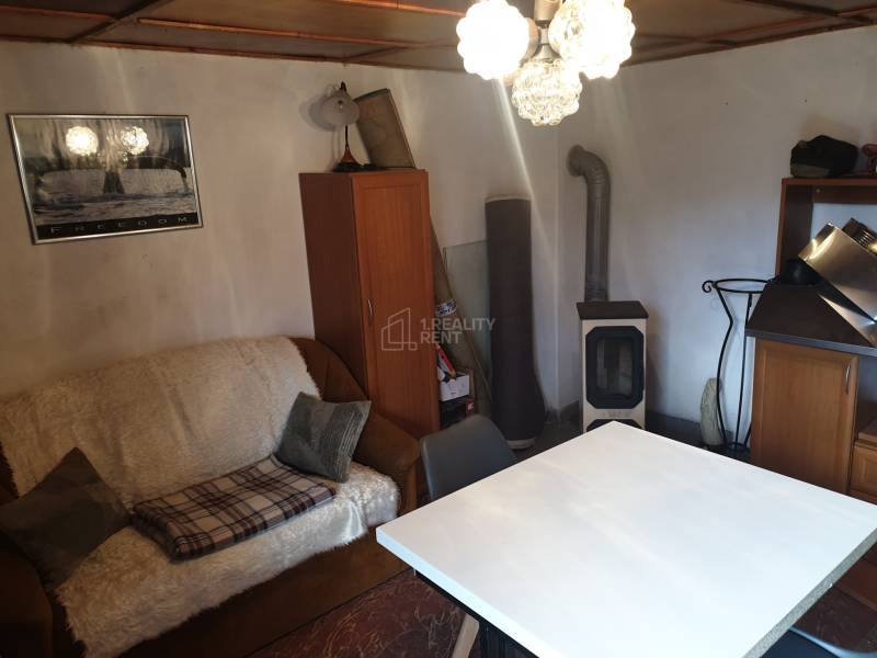 Living room in a cottage with a sofa, table, and wood stove.