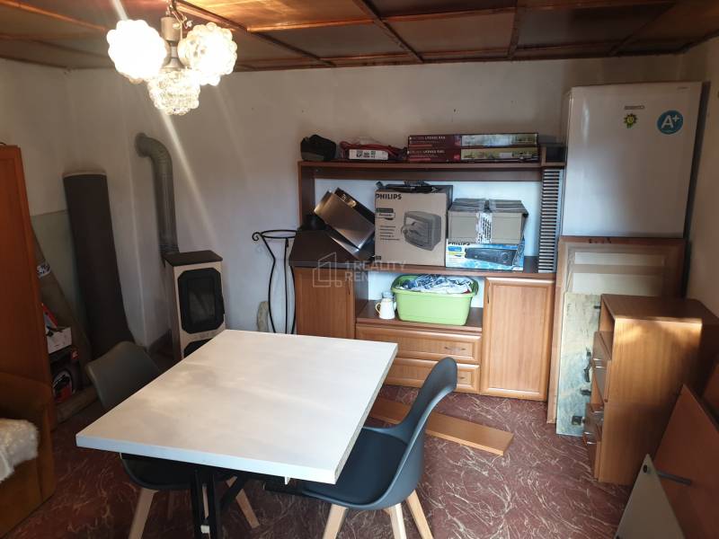 Small table, chairs, wardrobe, refrigerator, fireplace, shelves with items.