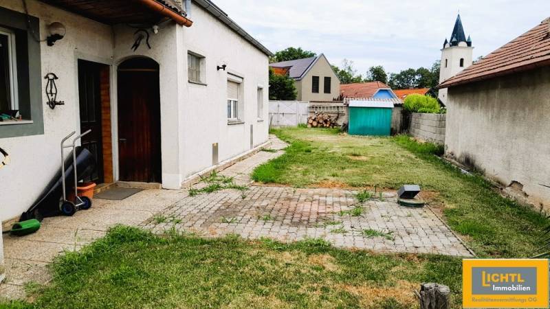 The courtyard of a family house in Potzneusiedl with a lawn, a garden shed, and a church tower in the background.