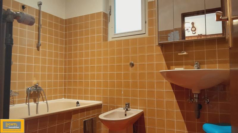 A bathroom with orange tiles in a family house, contains a bathtub, bidet, and sink.