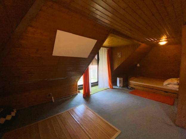 An attic room in a family house with wooden paneling and a bed on the right side.