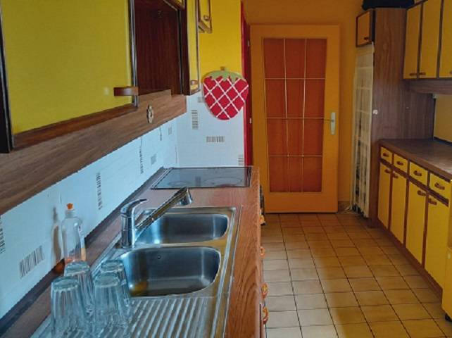 A kitchen in a family house with yellow cabinets and a stainless steel sink.