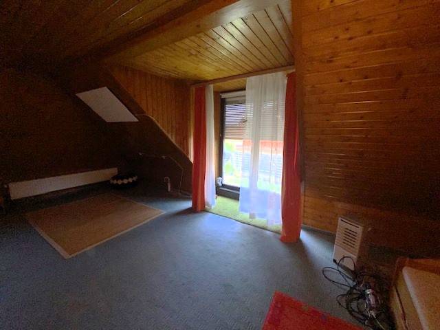 Attic room with wooden paneling in a family house, curtains over the window.