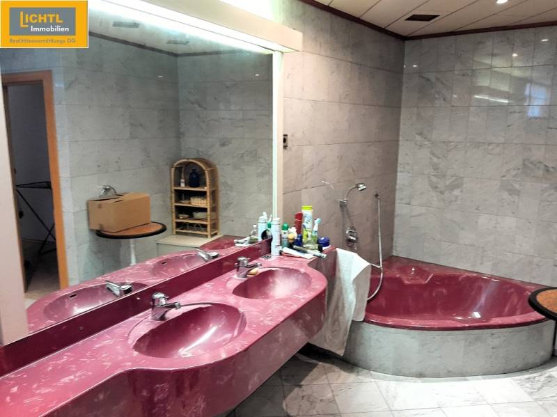 A bathroom with marble walls and a pink sink, next to a large bathtub.
