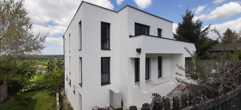 Villa in Hainburg an der Donau with a white facade, surrounded by greenery and a blue sky.