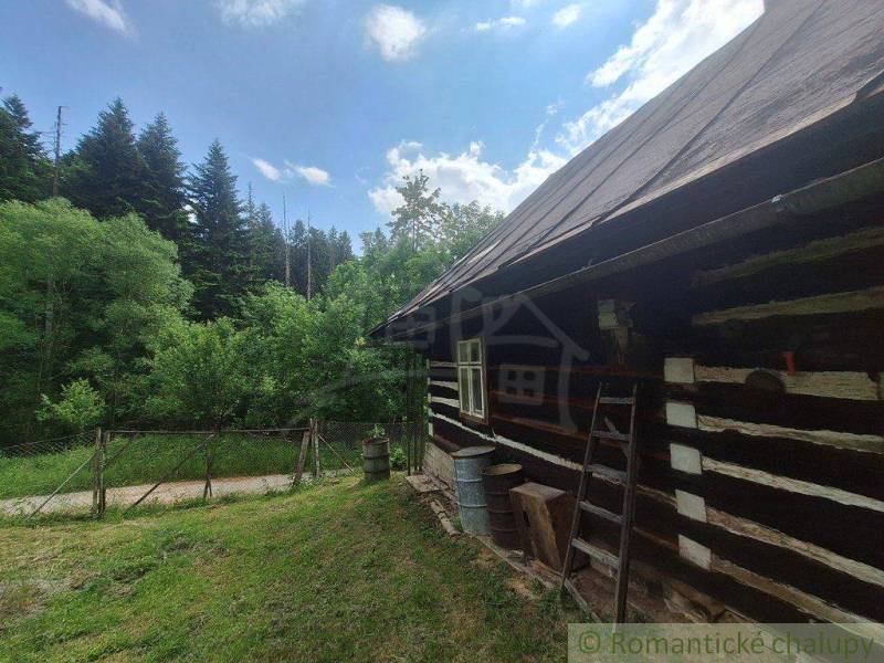 A cottage in Zákopčí surrounded by forest, wooden walls, a fence, and a blue sky.