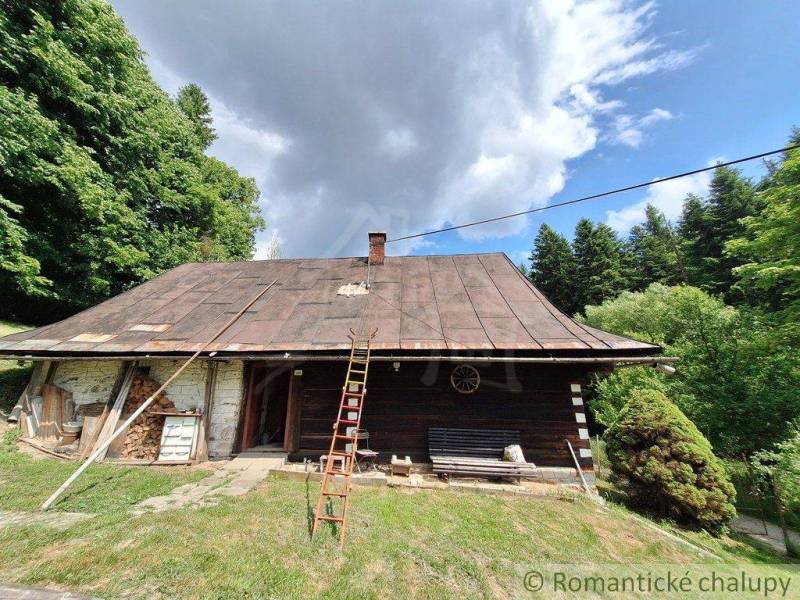 A rustic cottage in Zákopčie surrounded by forests and a dramatic cloud in the sky.