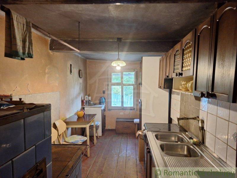 A kitchen in a cottage with a wooden floor, a tiled stove, and wooden cabinets.