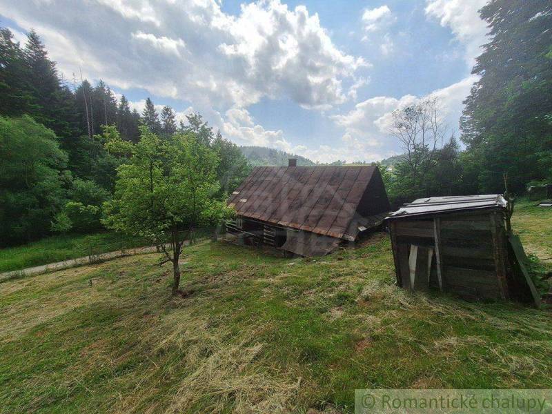 A wooden cottage in Zákopčie surrounded by forests and a blue sky.