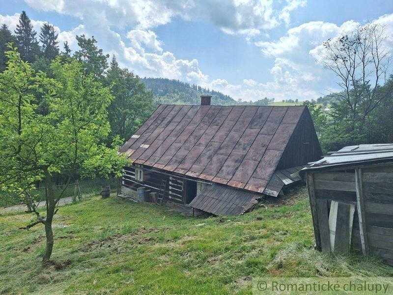A wooden cabin in Zákopčie on a slope, surrounded by trees and a blue sky.