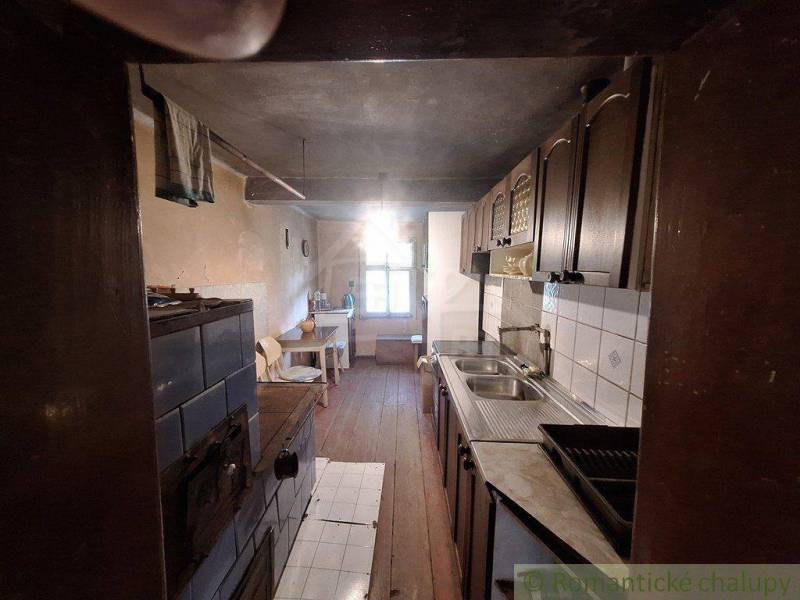 A kitchen in a cabin with wooden paneling, a tiled stove, and a sink.