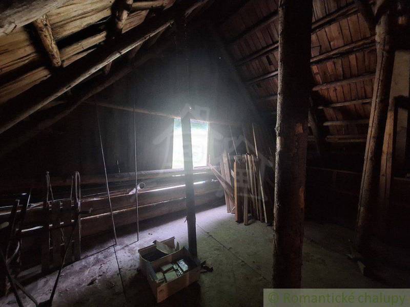 The attic of the cottage with wooden beams and a window illuminating the space.