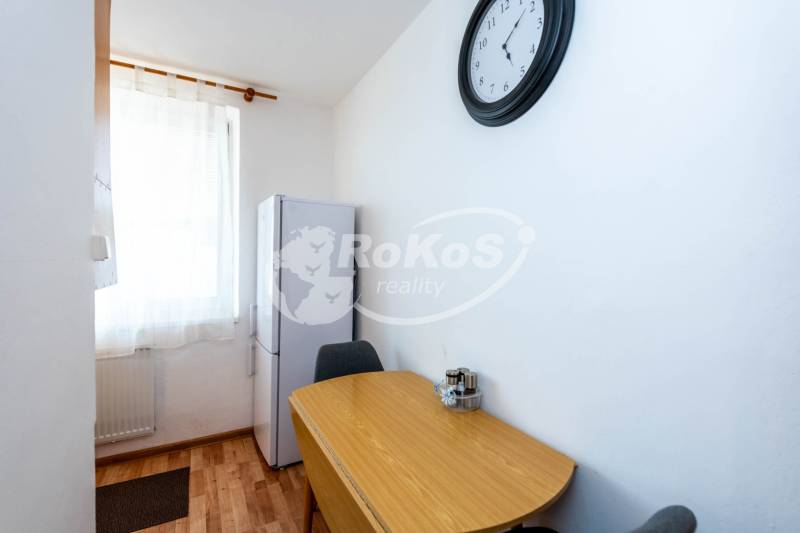 Dining table and refrigerator in a 2-room apartment with wall clock.