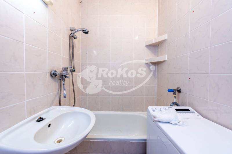 Bathroom in a 2-room apartment with a bathtub, sink, and washing machine, white tiles.