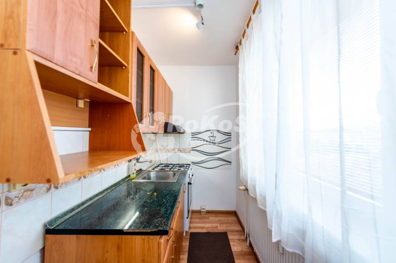 A kitchen unit with a white curtain and wooden cabinets in a 2-room apartment.
