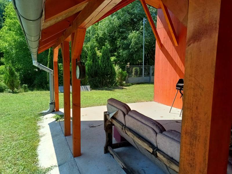A veranda at the cottage in Tužina with seating and a grill surrounded by greenery.