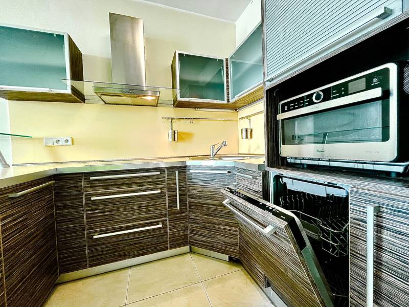 A kitchen in a 2-room apartment with stainless steel appliances and wooden cabinets.