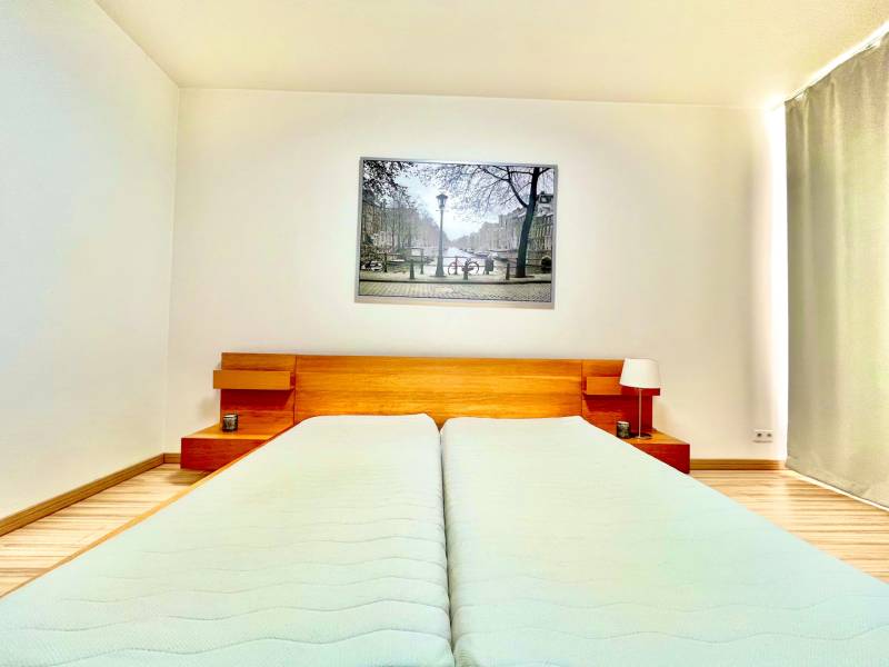 Bedroom with a double bed, wooden headboard, and a painting in a two-room apartment.