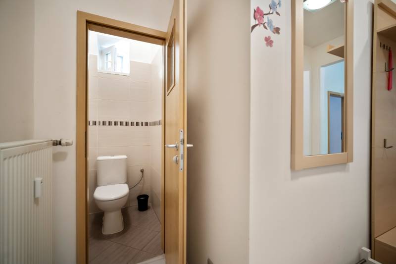 A toilet in a 3-room apartment with a window and white tiles.