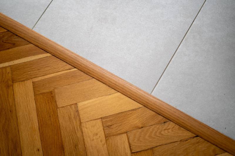 Transition between wooden flooring and white tiles in a three-room apartment.
