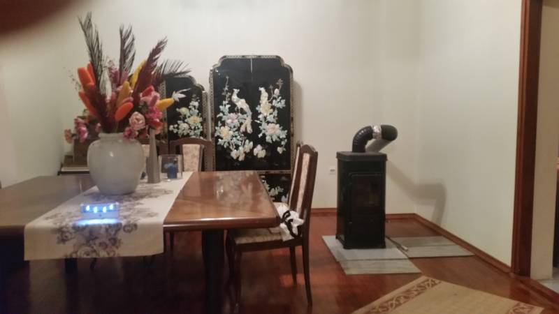 Interior of a family house with a wooden table, a tiled stove, and a decorative screen.