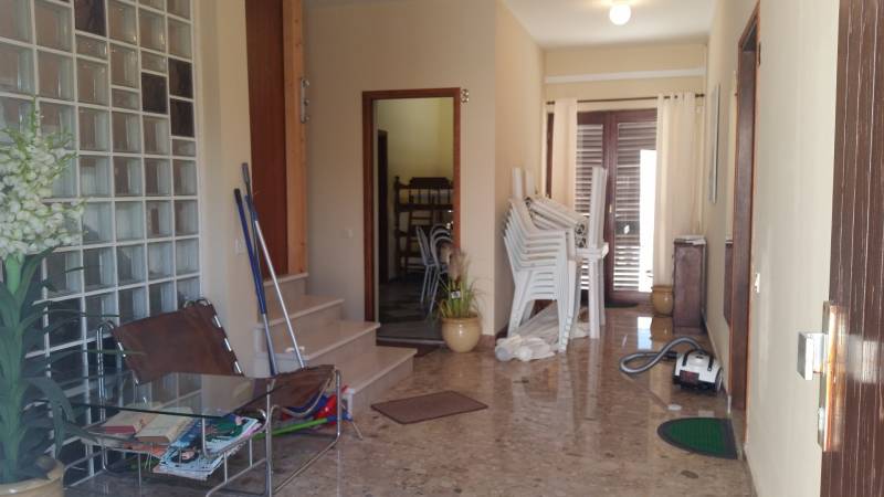 A hallway in a family house with stacked chairs, a glass table, and a vacuum cleaner.