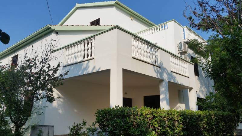 A family house in Vrsi with a white balcony and greenery in the surroundings.