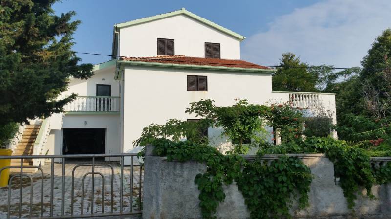 A family house in Vrsi with a white facade and a terrace surrounded by greenery.