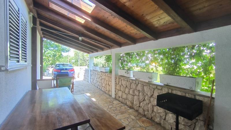 Covered terrace with a wooden table and grill in a family house in Vrsi.