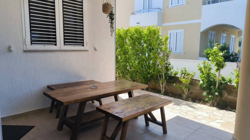 A wooden table with benches on the terrace of a family house in Vrsi, surrounded by greenery.